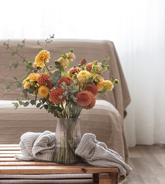 Eine Vase mit einem Strauß gelber und orangefarbener Chrysanthemen auf einem Tisch mit einem gestrickten Element im Inneren des Raumes.