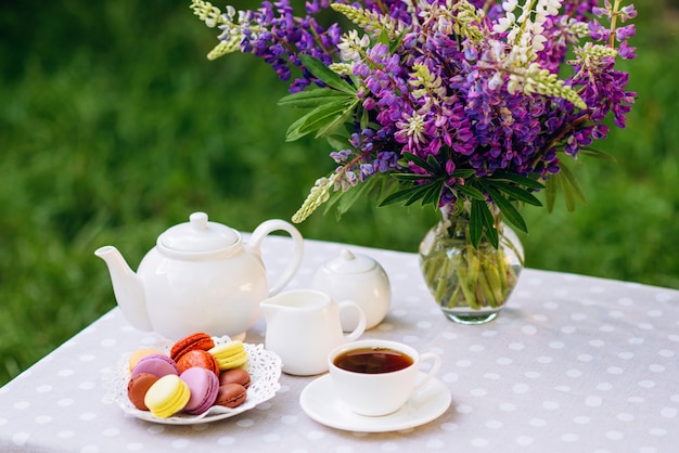 Eine Vase mit Lupinenblüten, eine Teekanne und eine Tasse Tee auf einem Holztablett