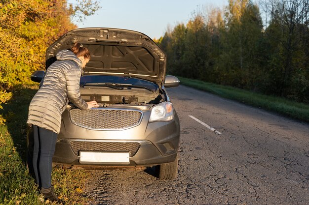 Eine verärgerte Frau steht in der Nähe ihres kaputten Autos und telefoniert im Herbst mit einem Handy auf der Straße.