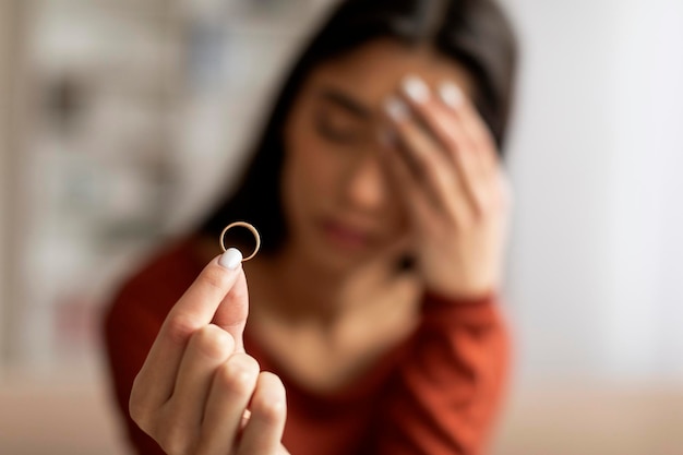 Eine verärgerte junge Frau hält mit einem schmerzhaften Gesichtsausdruck einen Hochzeitsring im Fokus