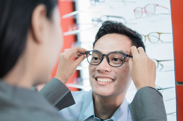 Eine Verkäuferin setzt einem männlichen Kunden bei einem Optiker eine neue Brille auf