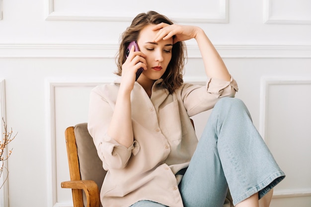 Foto eine verzweifelte millennial-frau erhält beunruhigende nachrichten während eines telefongesprächs und drückt traurigkeit aus, während sie sitzt