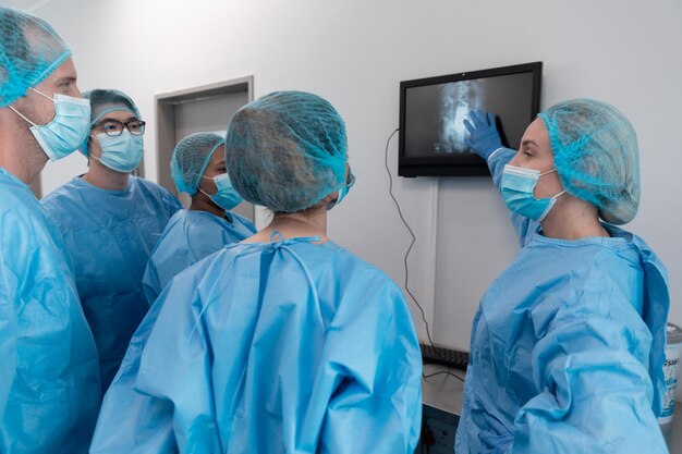 Eine vielfältige Gruppe männlicher und weiblicher Chirurgen im Operationssaal trägt Gesichtsmasken und blickt auf den Bildschirm