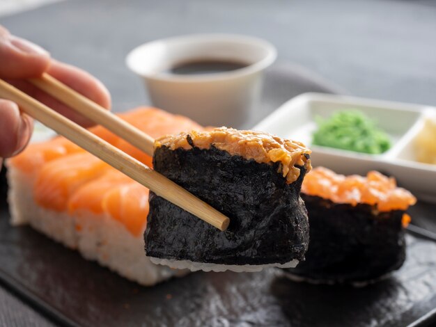 Eine Vielzahl von japanischen Brötchen und Sushi auf einem strukturierten schwarzen Teller. Seitenansicht. Bambusstöcke halten ein Gunkan. Nahaufnahme