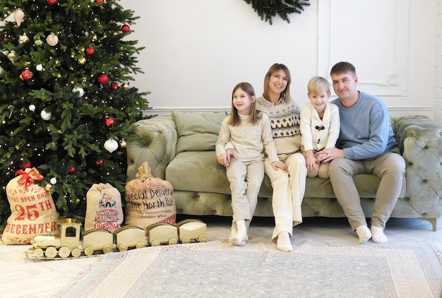 Eine vierköpfige Familie posieren auf einem Sofa in einem Wohnzimmer Weihnachtsdekor Familie lächelt und schaut in die Kamera