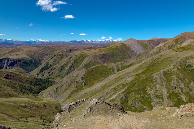 Eine völlig grüne Landschaft mit hohen felsigen Bergen unter einem strahlend sonnigen Himmel mit ein paar Wolken.