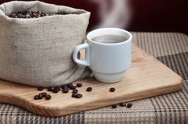 Eine volle Tüte braune Kaffeebohnen und eine weiße Tasse heißen Kaffee l