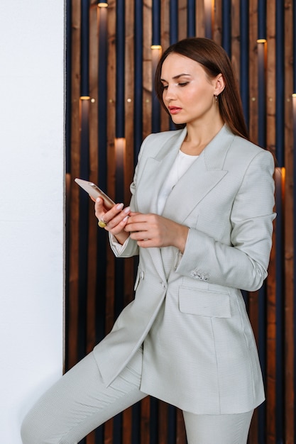 Eine vorbildliche Frau in einem Geschäftsanzug mit einem Telefon in ihren Händen. Kleidungsvorführung in einem Showroom