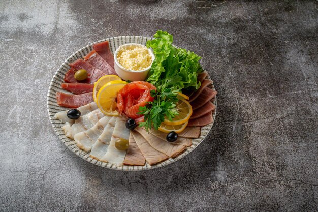 Eine Vorspeise in einem Restaurant, verschiedene Fleischsorten. Geschnittenes Fleisch und Wurst in Schichten auf einem Teller mit Grüns gegen einen grauen Steintisch