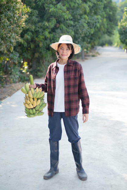 Eine weibliche Bauerin in einem roten Hemd steht und hält eine Gruppe Bananen in der Hand