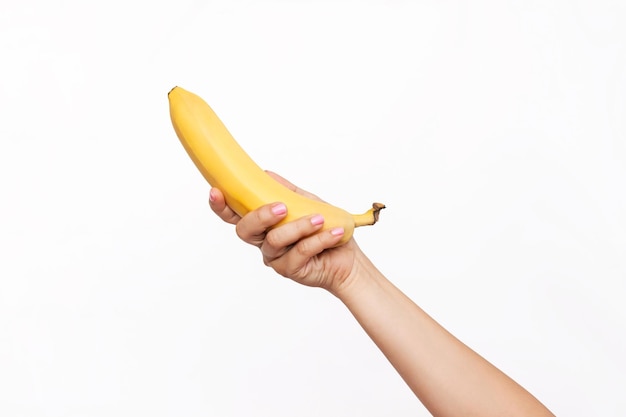 Eine weibliche Hand, die eine reife frische gelbe Banane lokalisiert auf einem weißen Hintergrund hält