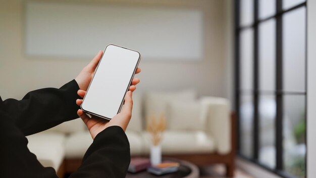 Eine weibliche Hand hält ein Smartphone-Modell über einem verschwommenen modernen Luxus-Wohnzimmer