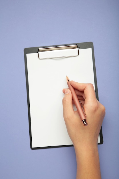Eine weibliche Hand hält einen Stift und eine schwarze Clipboard mit Papier auf lila Hintergrund Vertikalfoto