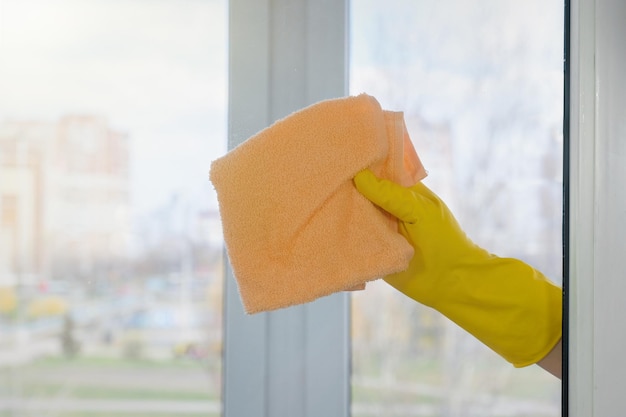 Eine weibliche Hand in einem gelben Handschuh wischt ein schmutziges Fenster ab Hausreinigung Haushaltskonzept