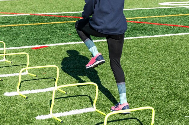 Foto eine weibliche highschool-läuferin führt laufübungen durch, indem sie über gelbe mini-hürden tritt