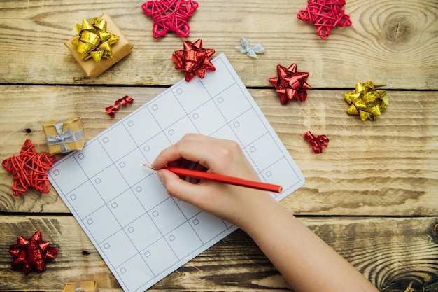 Eine Weihnachts-Komposition mit einem Segelflugzeug oder Kalender eine Frau an der Hand hält einen Bleistift Bögen und Geschenke auf einem hölzernen Hintergrund Das Konzept von Weihnachten und Neujahr