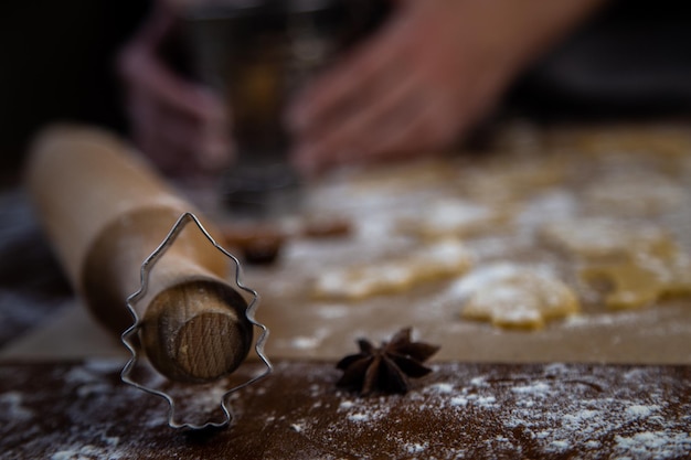 Eine weihnachtsbaumförmige Form steht auf einem Nudelholz gelehnt vor einem Hintergrund von Kekspergamen...