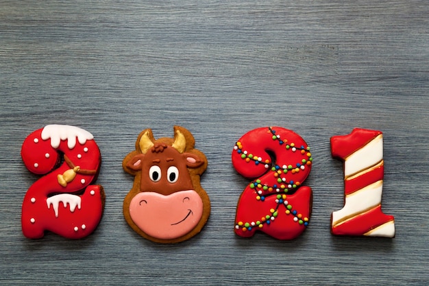 Eine Weihnachtskarte für die Feiertage. Lebkuchen in Form von Zahlen 2021 und das Symbol des Neujahrsbullen auf grauem Holzhintergrund. Frohe Weihnachten und ein neues Jahr.