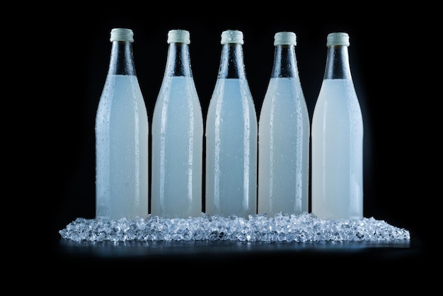 Eine weiße Flasche mit einem Sodagetränk auf Eis auf schwarzem Hintergrund