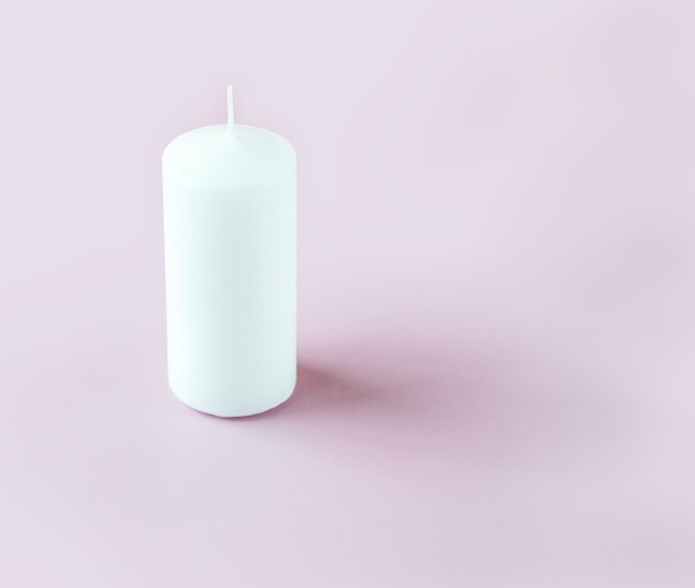 Eine weiße hohe Kerze auf dem hellrosa Hintergrund mit Kopienraum