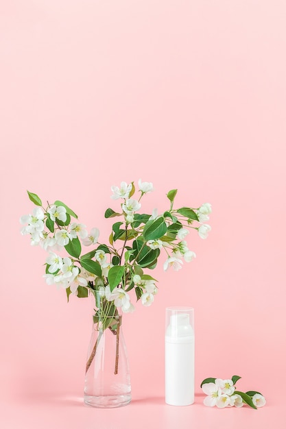 Eine weiße leere kosmetische Tube Flasche und blühender Zweig der Blume auf rosa Hintergrund