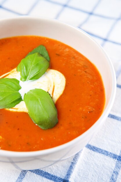 eine weiße Schüssel voller frischer Tomatensuppe mit Basilikumblättern obendrauf