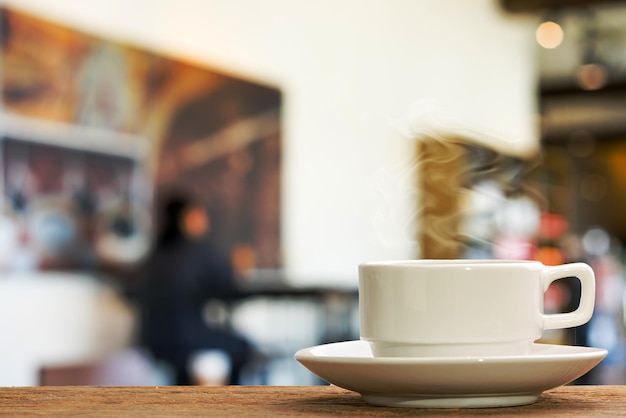 eine weiße tasse heißen kaffee auf dem tisch und unscharfer caféhintergrund.