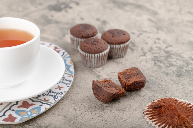 Eine weiße Tasse heißen Tee mit Schokoladenmuffins auf einem Steintisch.
