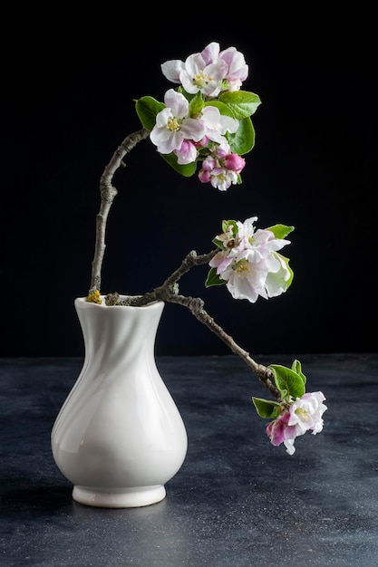 Eine weiße Vase mit einem Kirschblütenzweig darin.