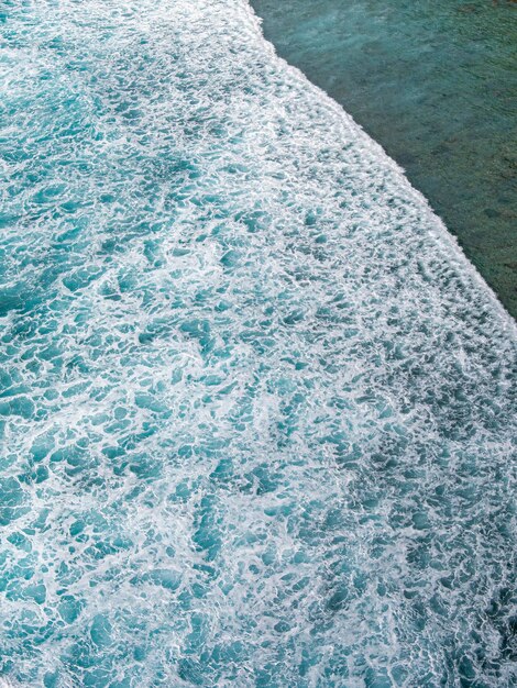 Eine Welle kracht am Ufer und das Meer ist blau.