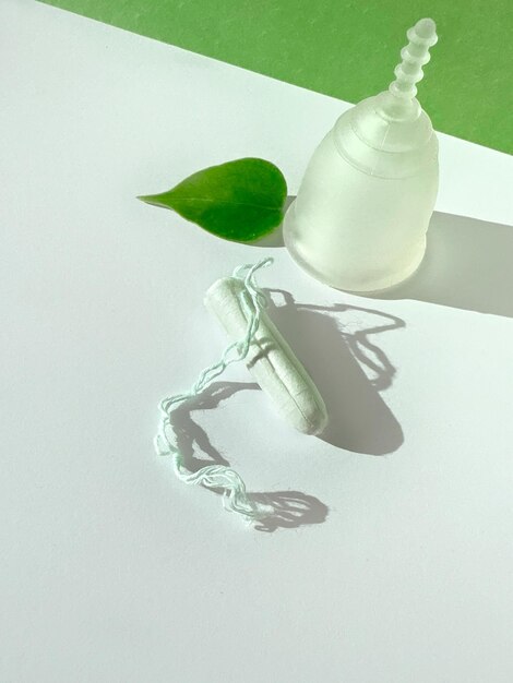 Foto eine wiederverwendbare silikon-menstruationskuppe und ein standard-tampon auf weißem und grünem papier