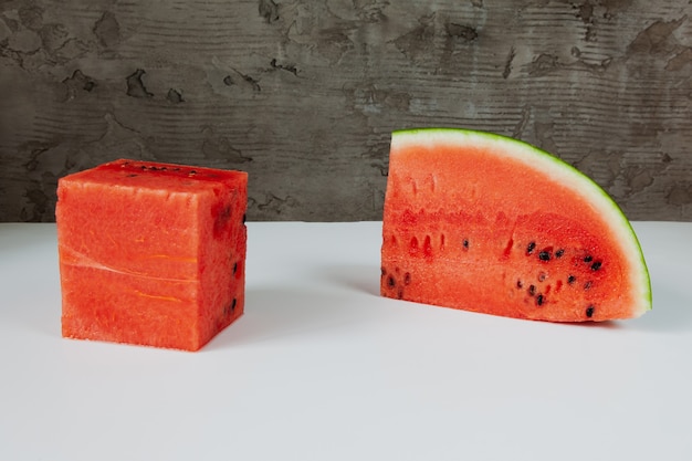 Eine würfelförmige Wassermelone auf einem weißen und grauen Betonhintergrund.