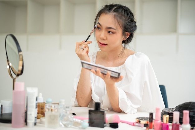 Eine wunderschöne asiatische Frau legt sich Augenschatten auf die Augenlider, um sich vorzubereiten