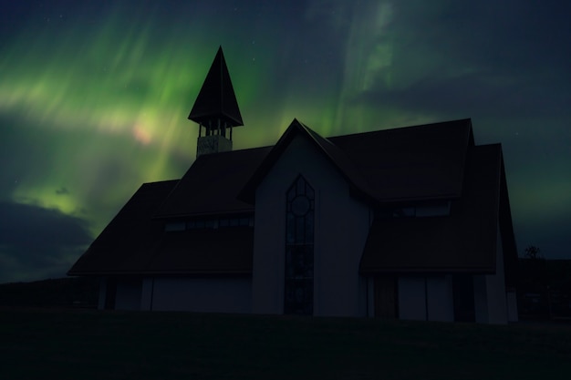 Eine wunderschöne traditionelle Kirche in der Nähe der Stadt Reykjavik eines Nachts mit einem wunderschönen Nordlicht. Island