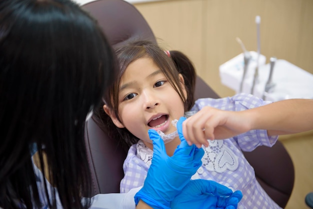 Eine Zahnärztin, die einem kleinen Mädchen in der Zahnklinik die Zahnuntersuchung und das Konzept der gesunden Zähne invisalign zeigt