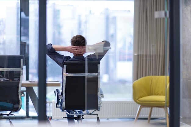 Eine Zeit zum Entspannen. Junger müder zufälliger Geschäftsmann, der am Schreibtisch in seinem Büro sich entspannt