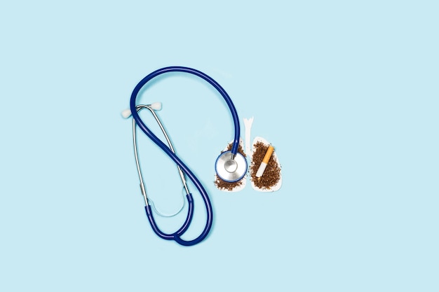 Eine zerbrochene Zigarette auf weißer Papierlunge und ein Stethoskop auf hellblauem Hintergrund mit Kopierraum