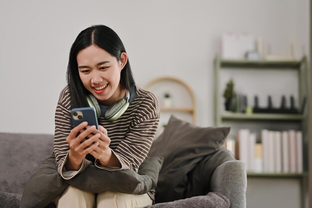 Eine zufriedene junge Frau schreibt SMS auf dem Handy und verbringt das Wochenende zu Hause