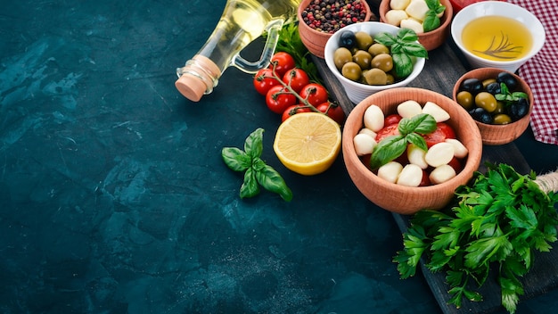 Einen Caprese-Salat kochen Mozzarella-Käse Kirschtomaten Oliven Basilikumblätter Öl Pfeffer Auf einem schwarzen Steintisch Freier Platz für Text