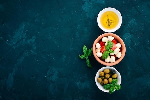 Einen Caprese-Salat kochen Mozzarella-Käse Kirschtomaten Oliven Basilikumblätter Öl Pfeffer Auf einem schwarzen Steintisch Freier Platz für Text