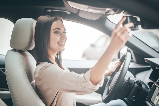 Einen Moment für dich. Junge attraktive Frau, die beim Autofahren lächelt und in den Rückspiegel schaut