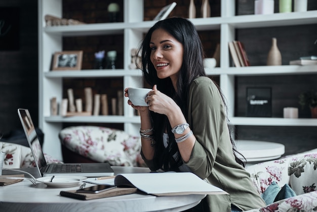 einen schönen Tag genießen. schöne junge Frau, die eine Tasse hält und mit einem Lächeln wegschaut