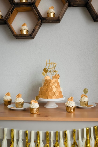 Einen süßen Tisch zum Geburtstag machen. Kuchen mit Waben, goldenes Design.