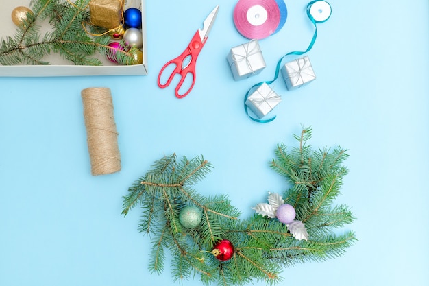 Einen Weihnachtskranz basteln. Fichtenzweig, Ornamente, Schere. Blauer Hintergrund.