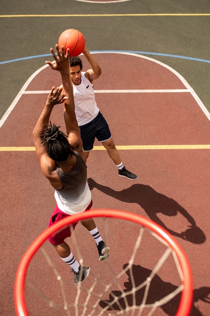 Einer der jungen interkulturellen Basketballspieler, die den Ball angreifen, während sein Rivale ihn werfen wird