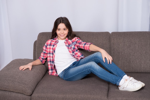 Einfach nur entspannen hier. Fühlen Sie sich auf dieser Couch wohl. Kindermädchen mit dem langen entspannenden Haar. Lieblingsort zum Entspannen zu Hause. Gemütliche Wohnatmosphäre. Unbeschwerte Kindheit. Bequeme Möbel. Entspanntes Kind.