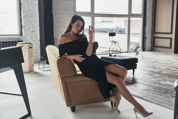 Foto einfach perfekt. attraktive junge frau im eleganten schwarzen kleid mit einem tiefen schlitz entspannt beim sitzen auf dem sofa