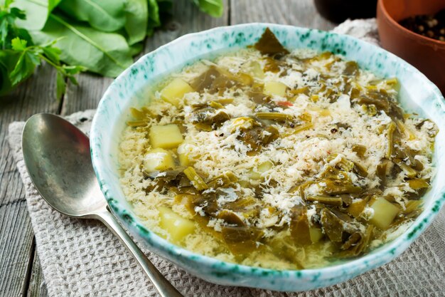 Einfache vegetarische Suppe aus Sauerampfer, Kartoffeln und geschlagenen Eiern auf einem alten Holzhintergrund.