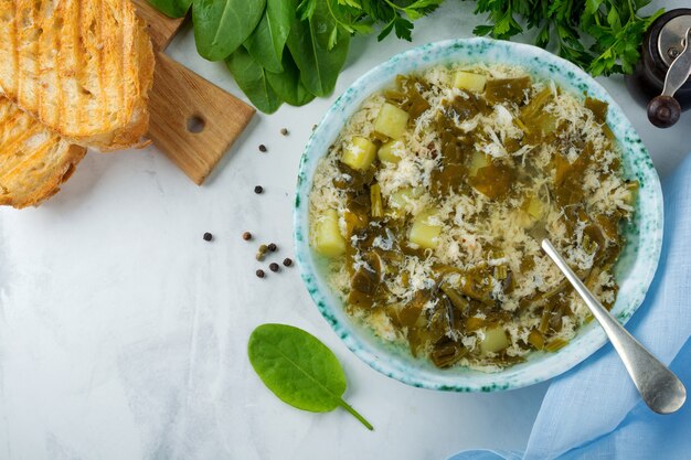 Einfache vegetarische Suppe aus Sauerampfer, Kartoffeln und geschlagenen Eiern auf einer hellen Oberfläche