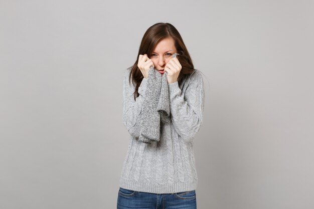 Einfrierende junge Frau in grauem Pullover in Schal isoliert auf grauem Wandhintergrund Studioportrait. Gesunder Modelebensstil, aufrichtige Emotionen der Menschen, Konzept der kalten Jahreszeit. Kopieren Sie Platz.